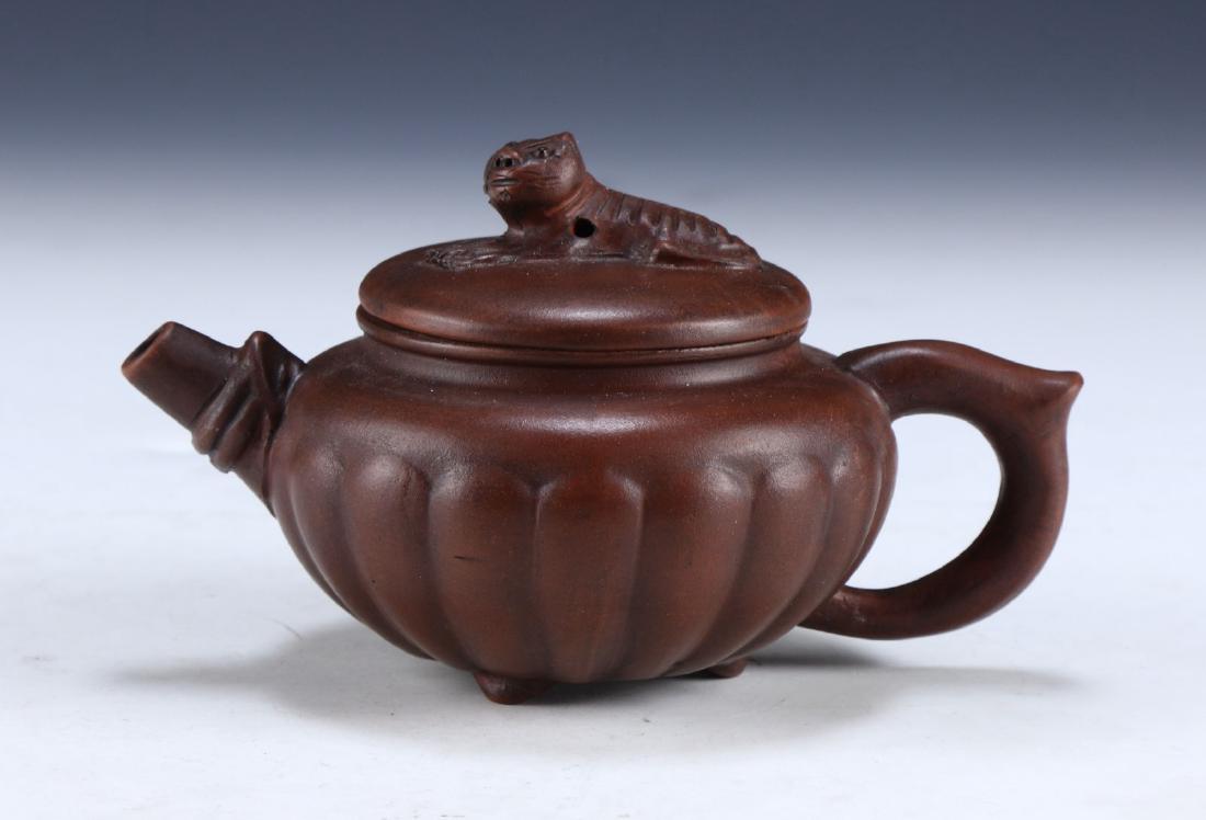 A CHINESE YIXING ZISHA TEAPOT: A Chinese Yixing Zisha Teapot: Of Compressed Globular Form, Rising From Three Splayed Feet To A Domed Lid, Four Character Mark On The Base Within A Square; Size: L: 5-1/4" (13.34cm)