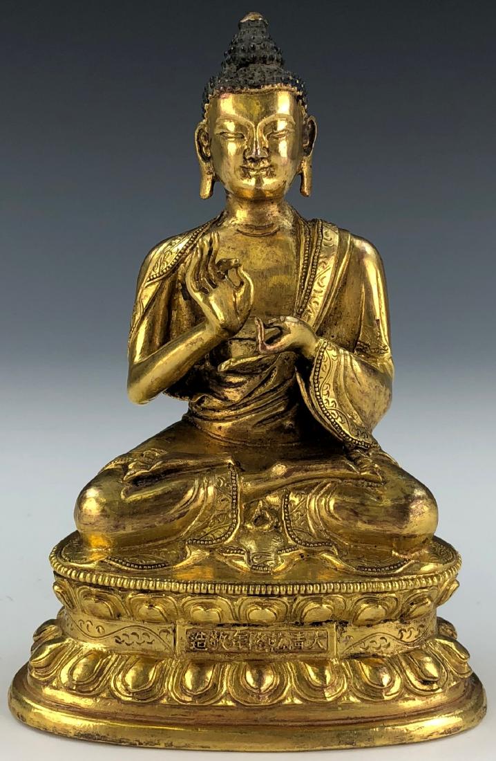 A TIBETAN GILT BRONZE BUDDHA: A Tibetan Gilt Bronze Buddha Figure: The Figure Is Shown Seated in Dhyanasana On A Double Lotus Plinth, Wearing A Robe Has Foliate Borders And Is Gracefully Draped Over The Shoulder And Around The Bod