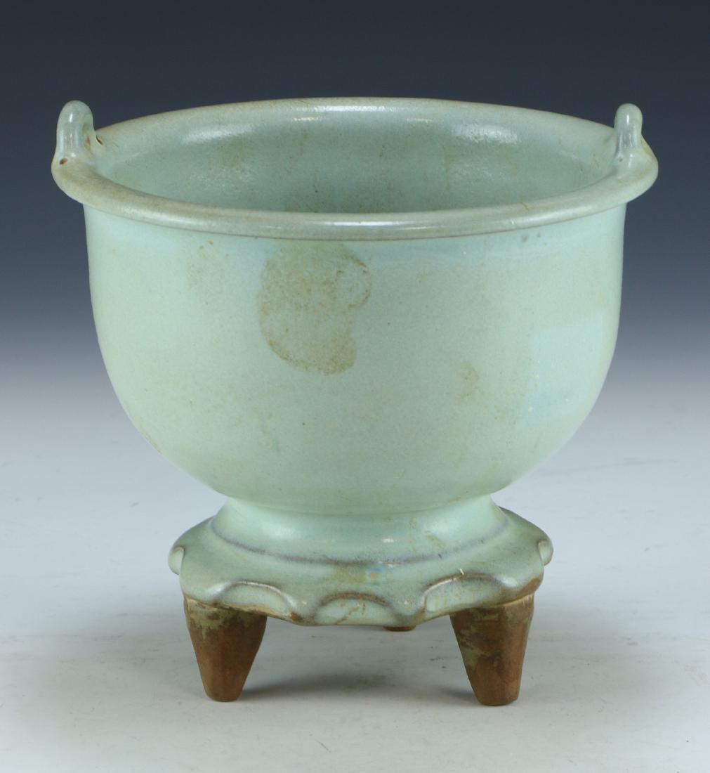 A CHINESE CELADON GLAZED TRIPOD PORCELAIN CENSER: A Chinese Celadon Glazed Tripod Porcelain Censer: Well Potted With Rounded Sides, Rising From A Base Rested On Three Pegged Feet To A Lipped Rim Flanked On Each Side By Arching Handles, Evenly Glazed 