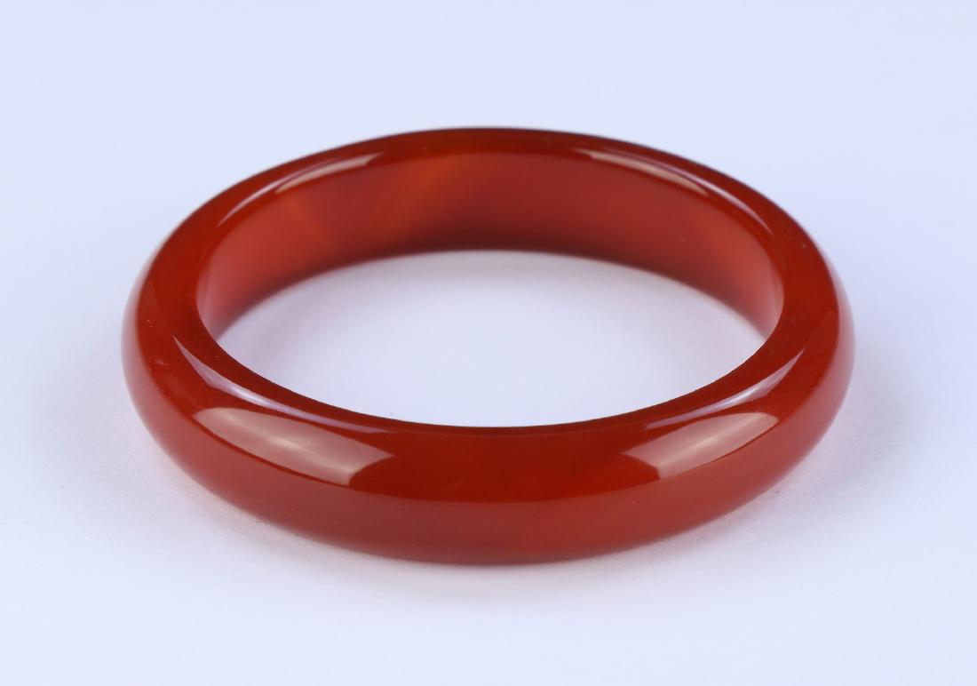 A CHINESE CARNELIAN AGATE BANGLE: A Chinese Carnelian Agate Bangle: Finely Carved And Polished, The Semi-Translucent Agate Body Of Mottled Deep Red Tones; Size: D: 3-1/4" (8.26cm)