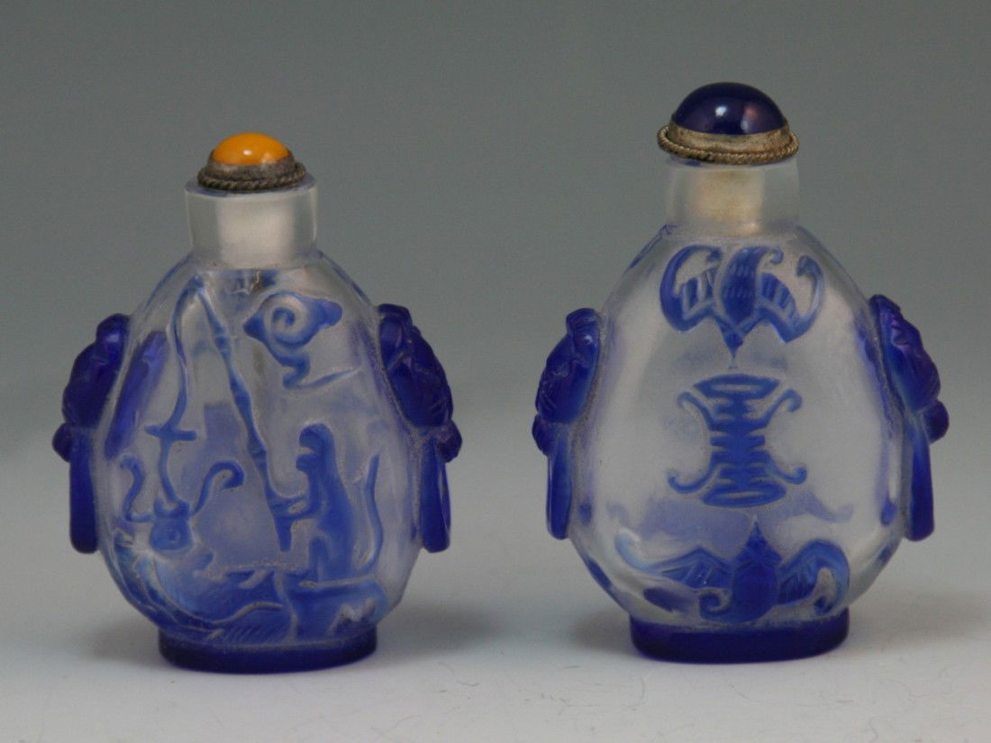 Two overlay glass snuff bottles: Two carved overlay Beijing glass snuff bottles: antique with design of bat and fish in blue on brilliant ground. With coral-glass and blue glass stoppers. Both 19th/20th century; H: 2-3/4"