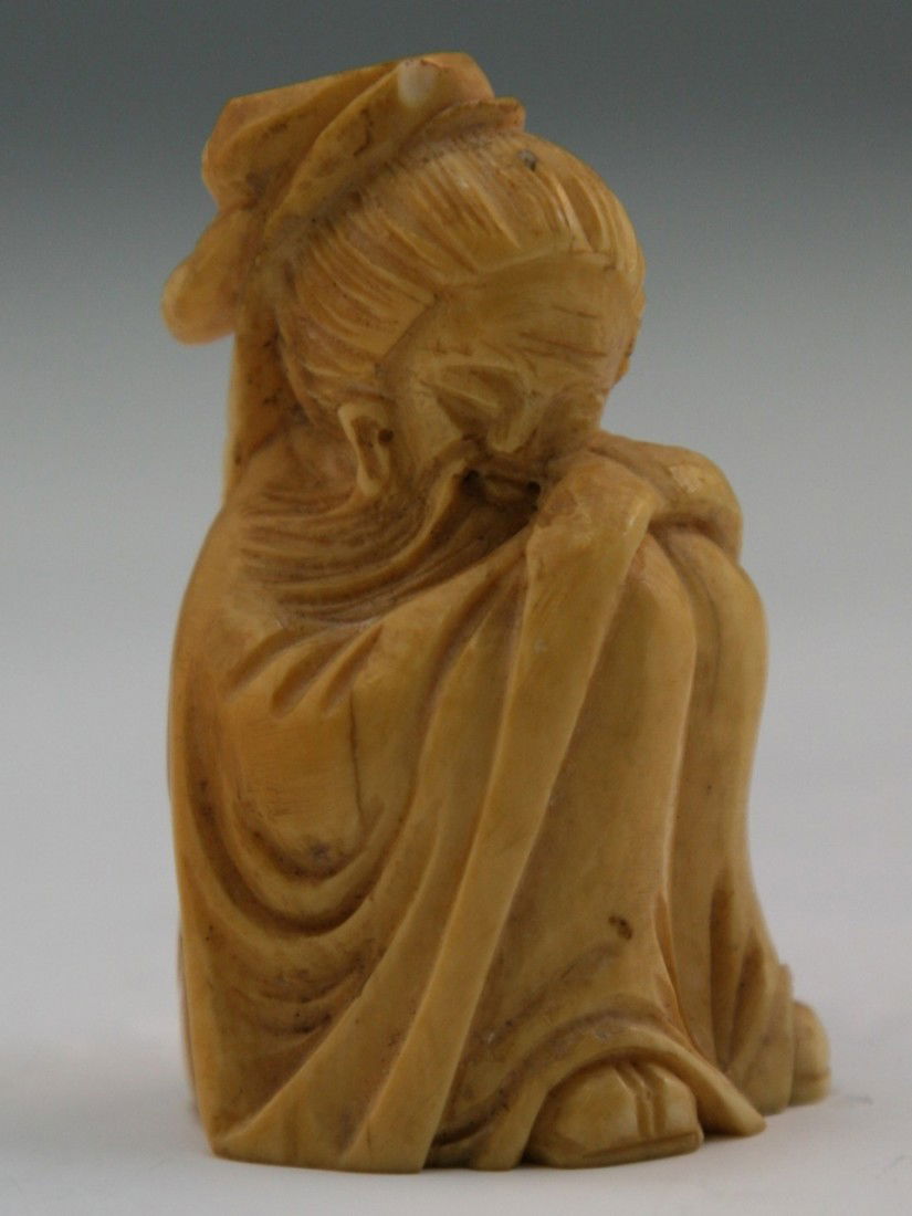Antique Carved Ivory Netsuke: Figure: Antique carved ivory netsuke: one older man with a long beard sitting down holding his knees up while dressed in a long robe; H: 2-1/4"