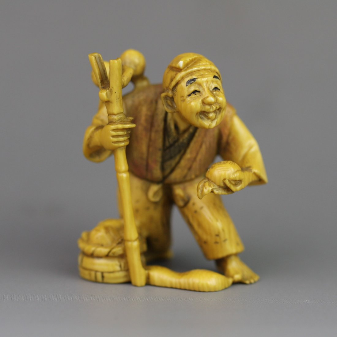 Antique Carved Ivory Netsuke: Fruit Picker: Antique carved ivory netsuke: one fruit picker standing with a piece of fruit in one hand while the other hand holds a long stick with fruit attached on the top: Tsugumitsu mark on the bottom: 19th ce