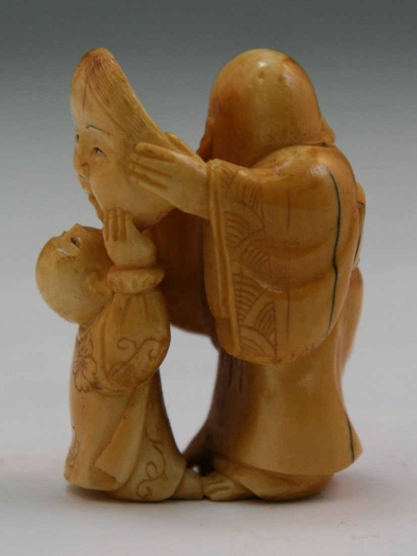 Antique Carved Ivory Netsuke: Figures: Antique carved ivory netsuke: one man holding a large mask of a woman out in front of him while a child looks up closely to kiss it; Size: H: 1-7/8"