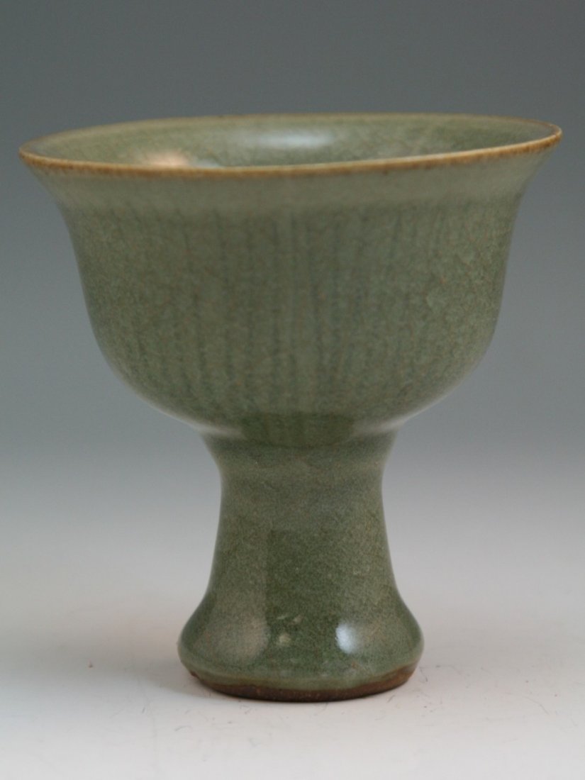 A Longquan Celadon Stemcup: A Longquan Celadon Stemcup: heavily covered overal inside and outside of the bell-shaped cup with a thick celadon glaze of deep olive-green tones suffused with crackles, base and footrim burnt sesame 