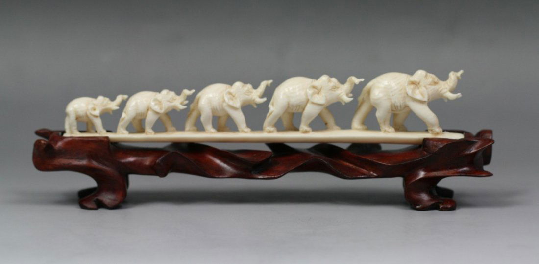 Finely Carved Ivory Elephant Bridge Group: Finely carved ivory elephant bridge group: of five richly caparisoned elephants in graduating sizes walking in a row: Most have trunk and tusk up in the air: on a custom carved wood stand; Size: L: 7-