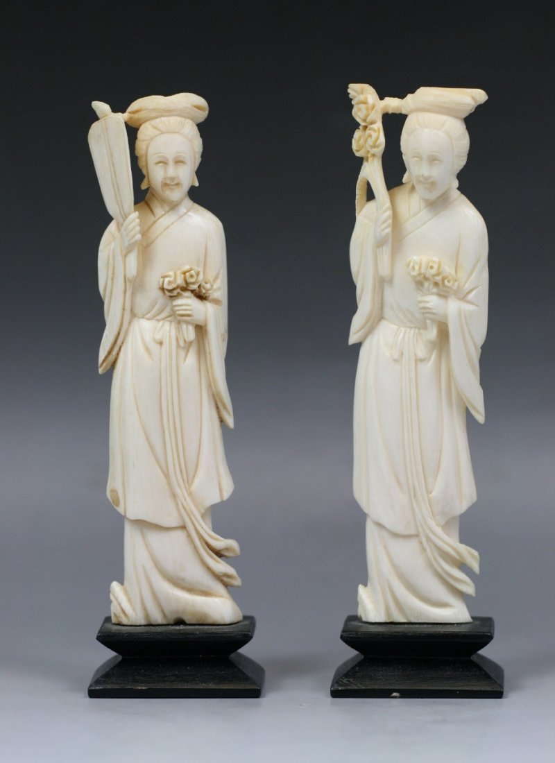 A Pair Of Antique Carved Ivory Beauties: A Pair of antique carved ivory beauties: both standing in flowing robes, one with a flowering branch in her right hand and a bouquet of flowers in her left hand, another with a fan in her right hand a