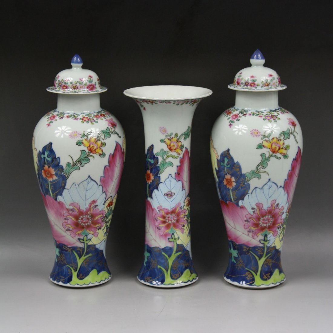 A Rare Qianlong Famille Rose Three-Piece Garniture: A Rare Qianlong Famille Rose Three-Piece Garniture: comprising one beaker vase and two baluster vases and covers, enamelled around the body and cover with tabacco leaves and blooming flowers, below a 