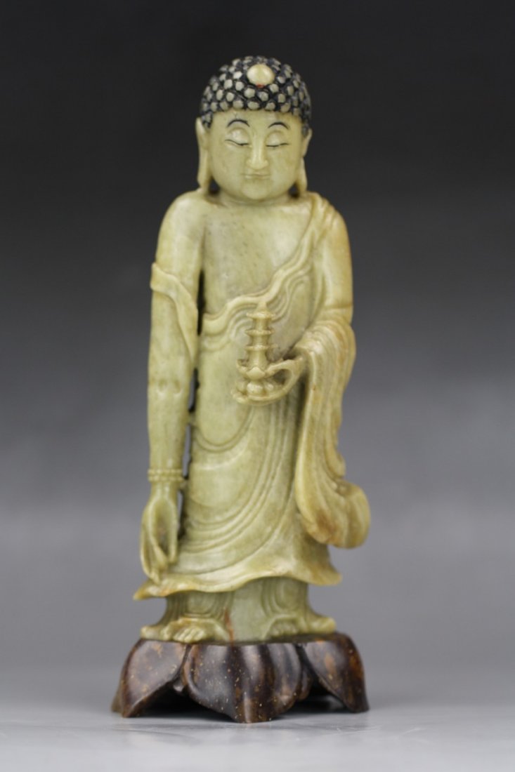 A Chinese Soapstone Carving Of Buddha: A Chinese Soapstone Carving Of Buddha: carved from the soapstone of celadon tone as a Buddha with long arms standing in flowing robes while carrying a miniature tower in hand, presented on a stone of 