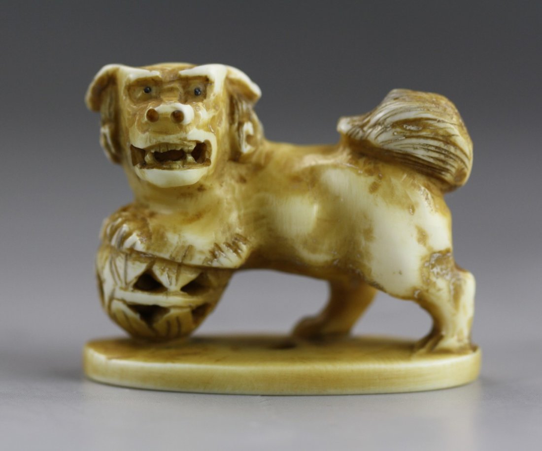 An Antique Ivory Netsuke: An Antique Ivory Netsuke: A ivory carved Shi-shi standing on a base with its front legs resting on a ball. Signed on the bottom of the base; Size: H: 1-1/2"