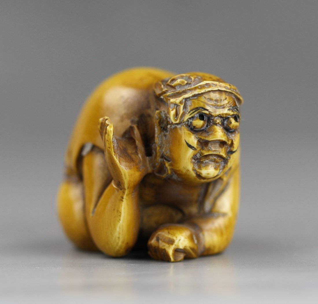 An Antique Ivory Netsuke: Figure: An Antique Ivory Netsuke: A man sitting down on his knees and elbows with one hand open while he looks forward. Signed on the bottom of the base; Size: H: 1-1/4"