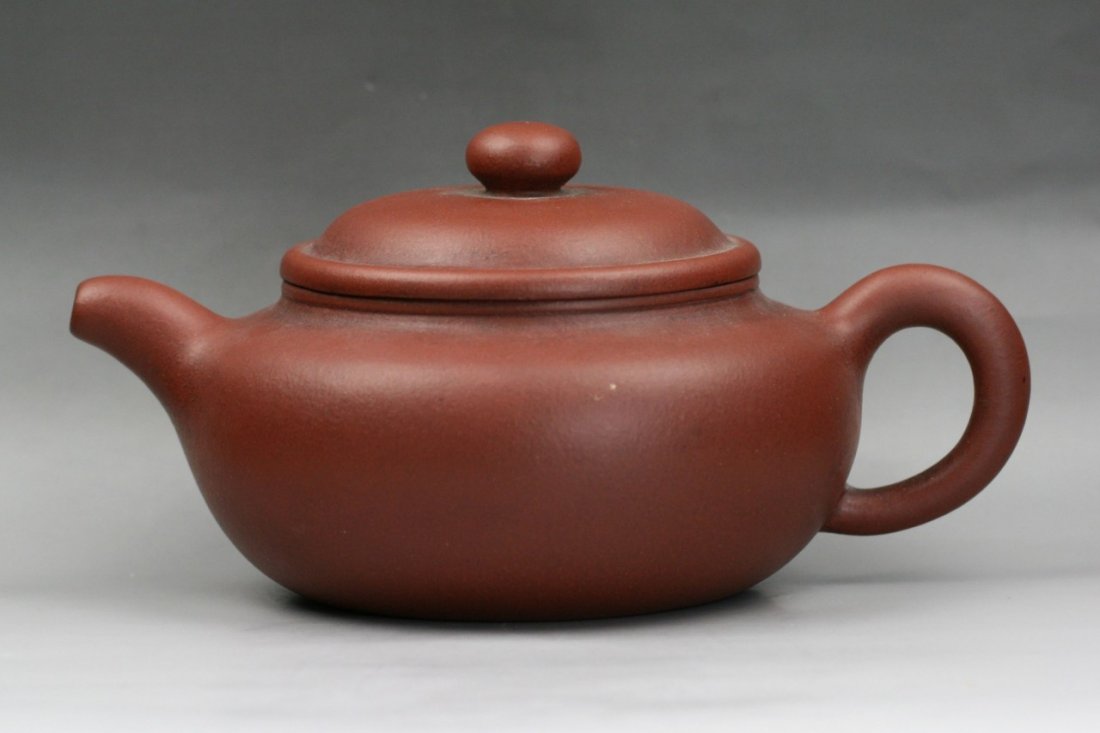 A Chinese Yixing Zisha Teapot By Gu Jingzhou: A Yixing Purple Clay Zisha Teapot By Gu, Jingzhou: of compressed globular form, with a loop handle opposite the short cylindrical spout, the fitted rounded cover with knob, with the seal of the potter