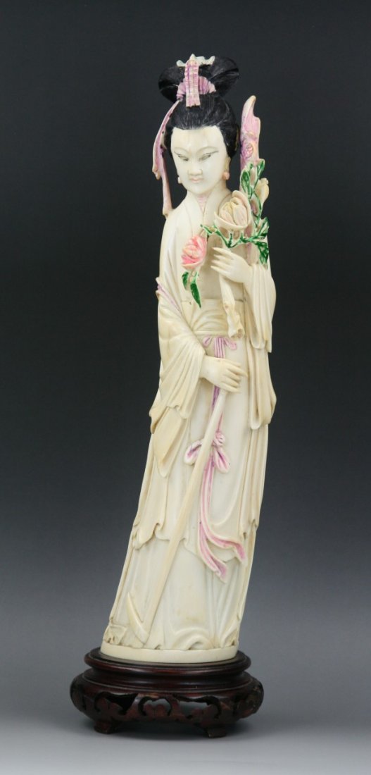 A Chinese Carved Polychrome Ivory Beauty: A Chinese Carved Polychrome Ivory Beauty: of a beauty standing in layered robes while holding a big flower branch in her hands, presented on wood stand; Size: H: 15-3/4" (40cm)
