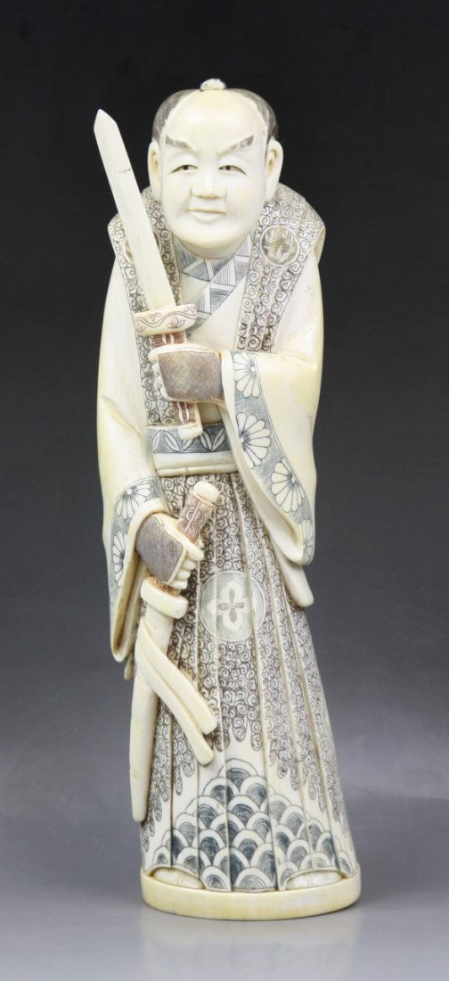 A Japanese Carved Polychrome Ivory Warrior: A Japanese Carved Polychrome Ivory Warrior: carved as a warrior standing in finely decorated robes while carrying swords in his hands, signed on the base; Size: H: 10"