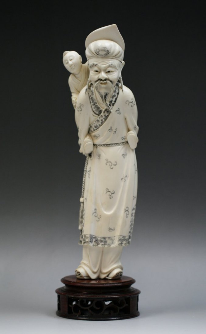 A Chinese Ivory Statue Of Scholar With Kid: A Chinese Ivory Statue Of Scholar With Kid: well carved as a scholar standing in flowing and decorated robes with a kid on his back, on dark wood stand, of Minguo Period; Size: H: 11"