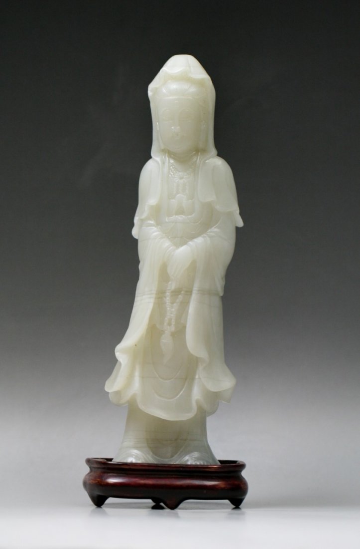 A Chinese Carved White Jade/Stone Guanyin: A Chinese Carved White Jade/Stone Guanyin: well carved from the stone with mute white color as Guanyin standing in flowing robes, presented on wood stand; Size: H: 8-3/8"; (overall) H: 9-1/8"
