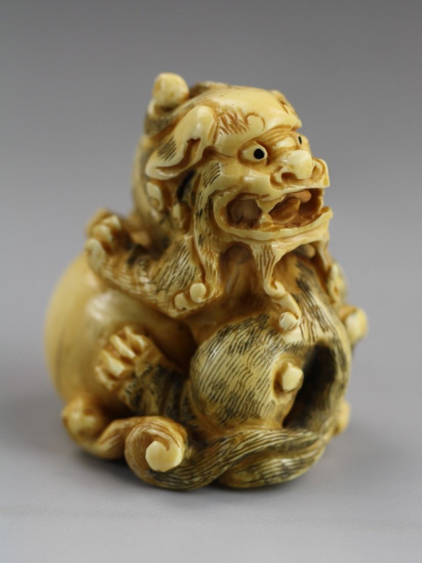 An Antique Ivory Netsuke: Shi-shi: an Antique Ivory Netsuke: A antique Shi-shi, Shi-shi is seated on a large ball while looking backwards. Signature is located on the bottom of the ball; Size: H: 1-7/8"
