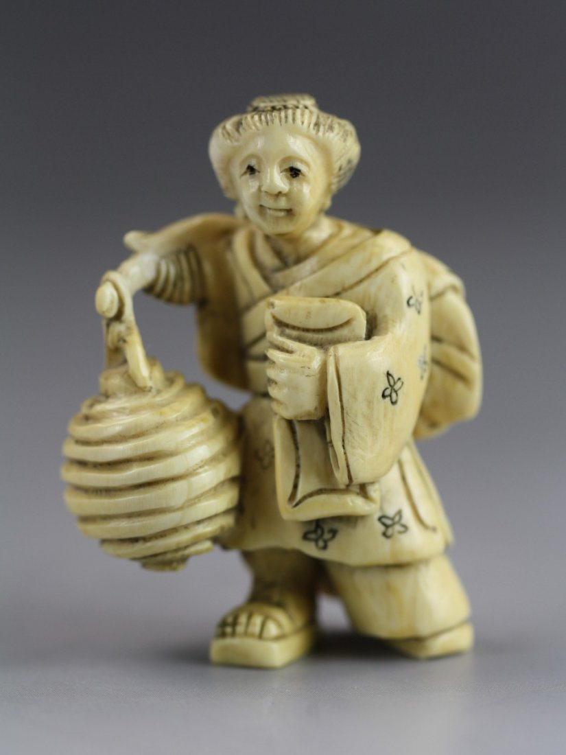 An Antique Ivory Netsuke: Lady: An Antique Ivory Netsuke: A elderly ivory women, carrying a few items in her left arm and over her back. She has a honey nest on the end of a stick. Signature on her right foot; Size: H: 1-7/8"