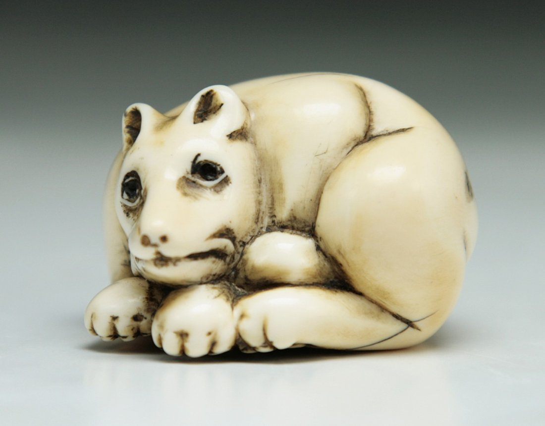 A Carved Antique Ivory Netsuke: 象牙根付 A Carved Antique Ivory Netsuke: of a puppy rested on its legs, with inlaid eyes, early 19th Century, signed on the base; Size: L: 1-1/4"