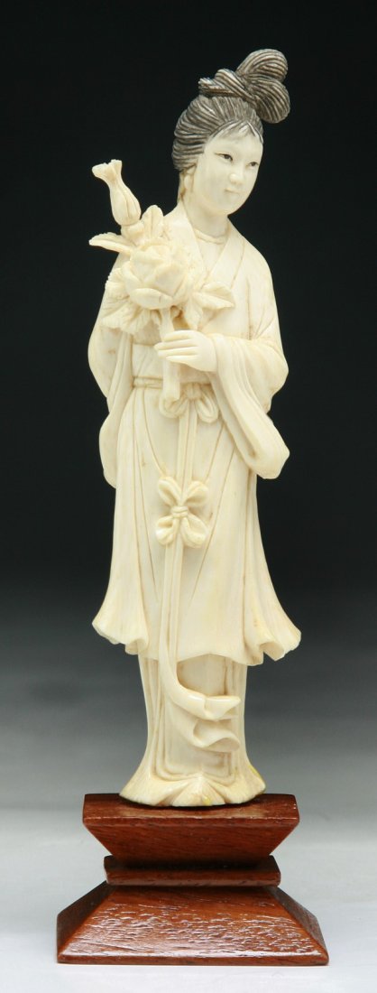 A Chinese Antique Carved Ivory Beauty: A Chinese Antique Carved Ivory Beauty: carved as a beauty standing in flowing robes carrying a blossom branch, presented on a wood stand; Size: H: 6"