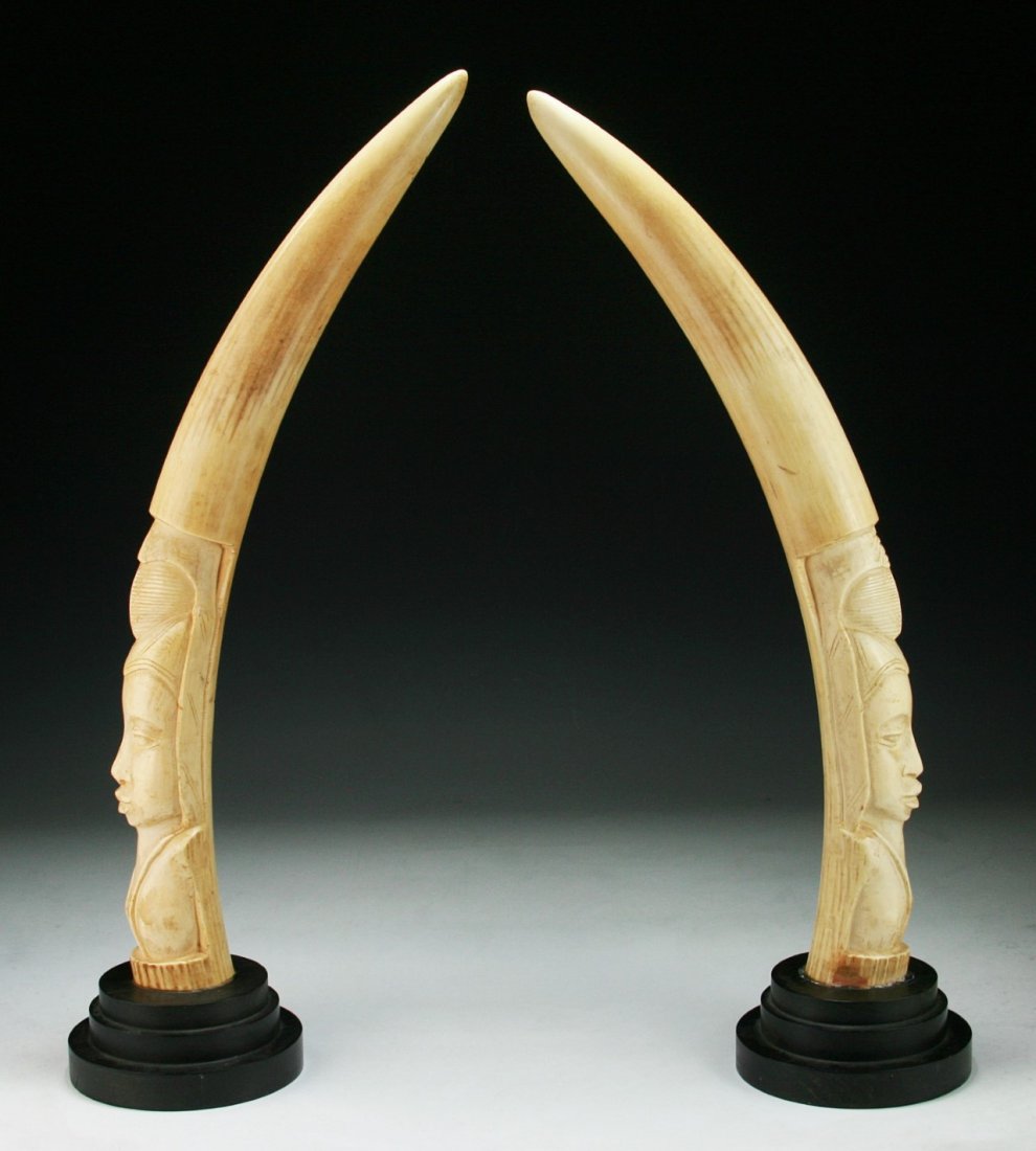 Pair Antique African Carved Ivory Tusks With Stands: Pair Antique African Carved Ivory Tusks With Stands: well polished tusks carved with figure faces, both on hardwood stands; Size: H: 23-1/2" (along curve); (overall) H: 26-1/2"