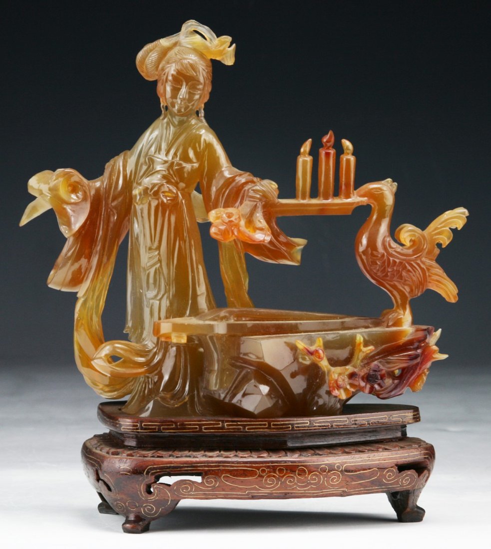 A Chinese Antique Carnelian Agate Beauty: A Chinese Antique Carnelian Agate Beauty: finely carved as a beauty in flowing robes holding a tray of lit candles as a bird stands to hold one side, presented on a wood stand, of Qing Dynasty; Size: 