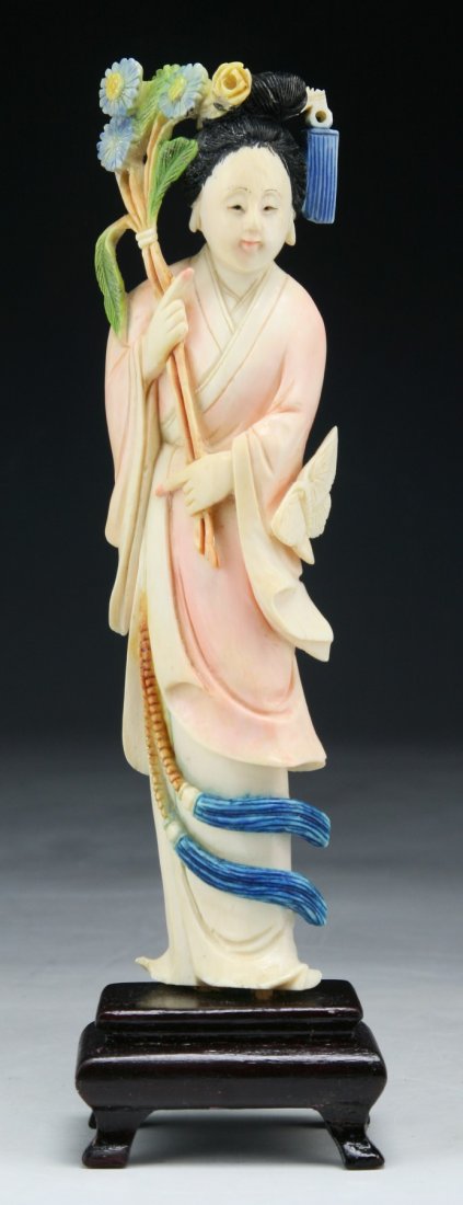 A Chinese Antique Polychrome Ivory Beauty: A Chinese Antique Polychrome Ivory Beauty: finely detailed beauty standing in swaying robes holding flowers in both hands; presented on a wood stand; Size: H: 7"; (overall) H: 8"