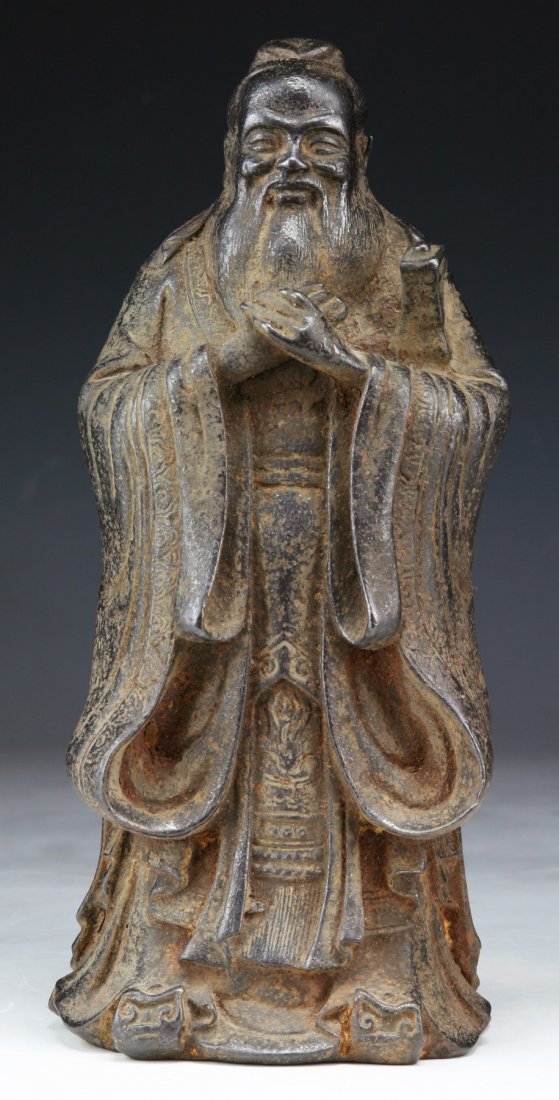 A Chinese Ming Dynasty Iron Figure Of A Scholar: A Chinese Ming Dynasty Iron Figure Of A Scholar: The bearded figure is cast in standing position with two hands raised before him, he wears a long robes belted at the waist, of 17TH Century; Size: H: 