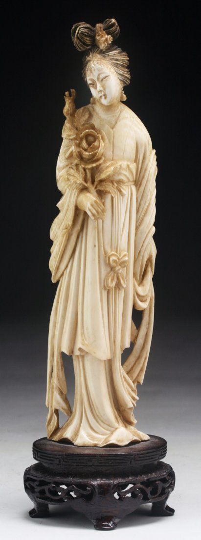 A Chinese Antique Carved Ivory Beauty: A Chinese Antique Carved Ivory Beauty: finely carved as a beauty in long flowing robes holding a blooming branch with her right hand, attached on a wood stand with openwork, African ivory, Late Qing D
