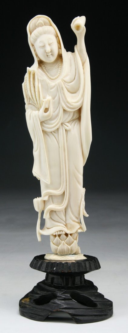 A Chinese Antique Carved Ivory Guanyin: A Chinese Antique Carved Ivory Guanyin: finely carved as Guanyin in long flowing robes standing on a lotus plinth, presented on a wood stand, African ivory, Late Qing Dynasty (19th Century), NO INTERN