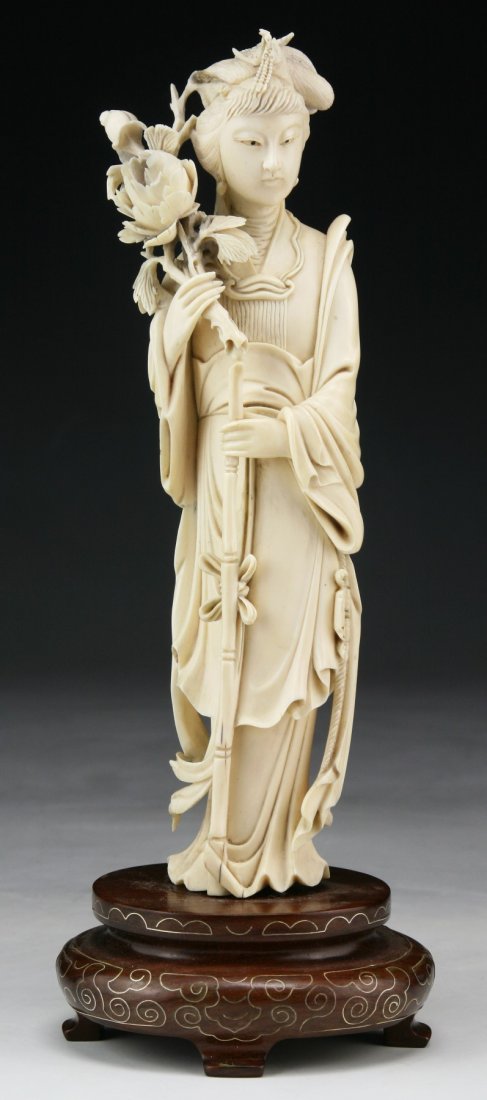 A Chinese Antique Ivory Beauty: A Chinese Antique Ivory Beauty: finely carved as a beauty in long flowing robes holding a blooming flower branch with her right hand and a long bamboo stick in the other, presented on wood stand, Asia