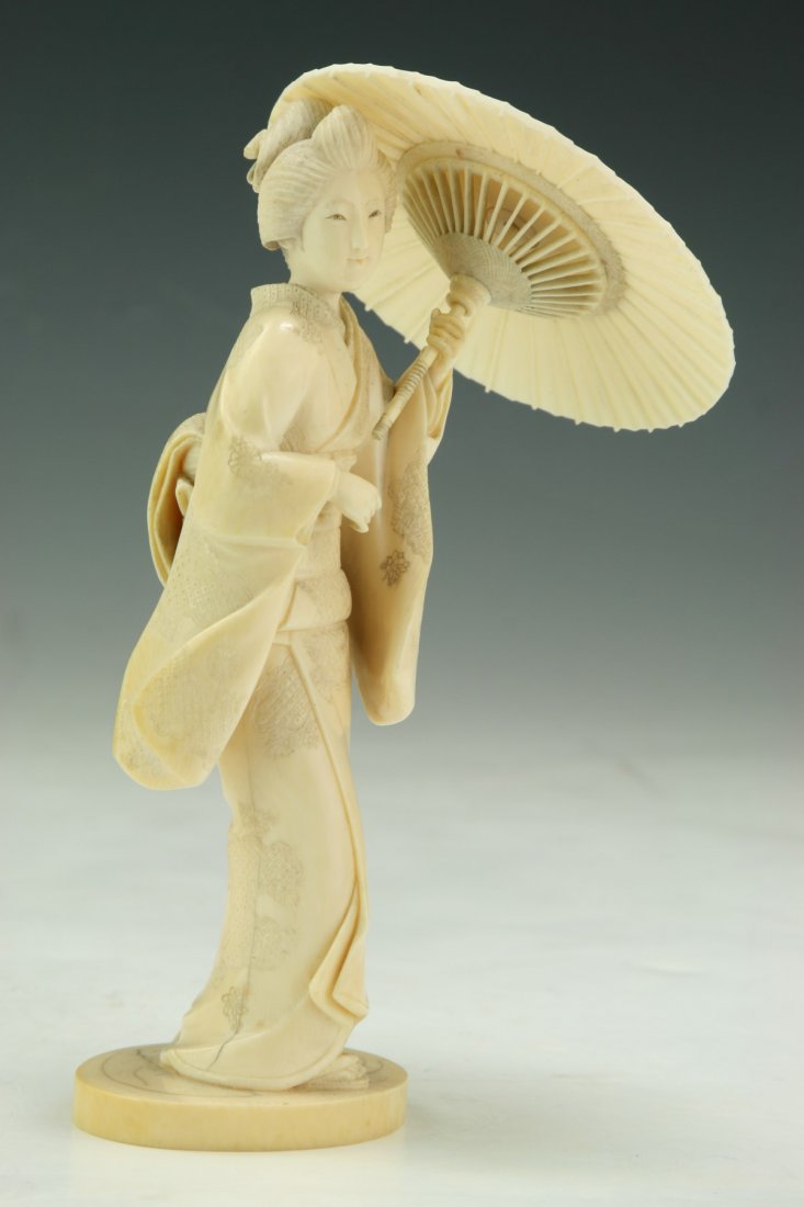 A Japanese Antique Ivory Carved Beauty: A Japanese Antique Ivory Carved Beauty: finely carved as a woman in a layered decorative Kimono holding an open umbrella with her left hand, African ivory, Meiji Period (Late 19th Century; NO INTERNAT