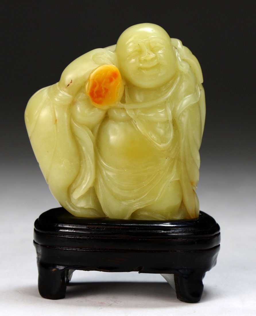 A Chinese Soapstone Carved Buddha: A Chinese Soapstone Carved Buddha: of natural creamy tones with some russet, finely carved as a laughing Buddha, presented on a wood stand; Size: H: 2-3/4"; (overall) H: 3-3/4"