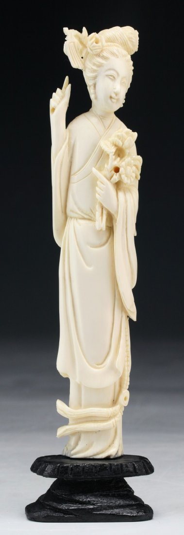 A Chinese Antique Carved Ivory Beauty: A Chinese Antique Carved Ivory Beauty: finely carved beauty standing in a long flowing robe holding flowers, presented on a wood stand, African ivory, Late Qing Dynasty (19th Century), NO INTERNATIONA