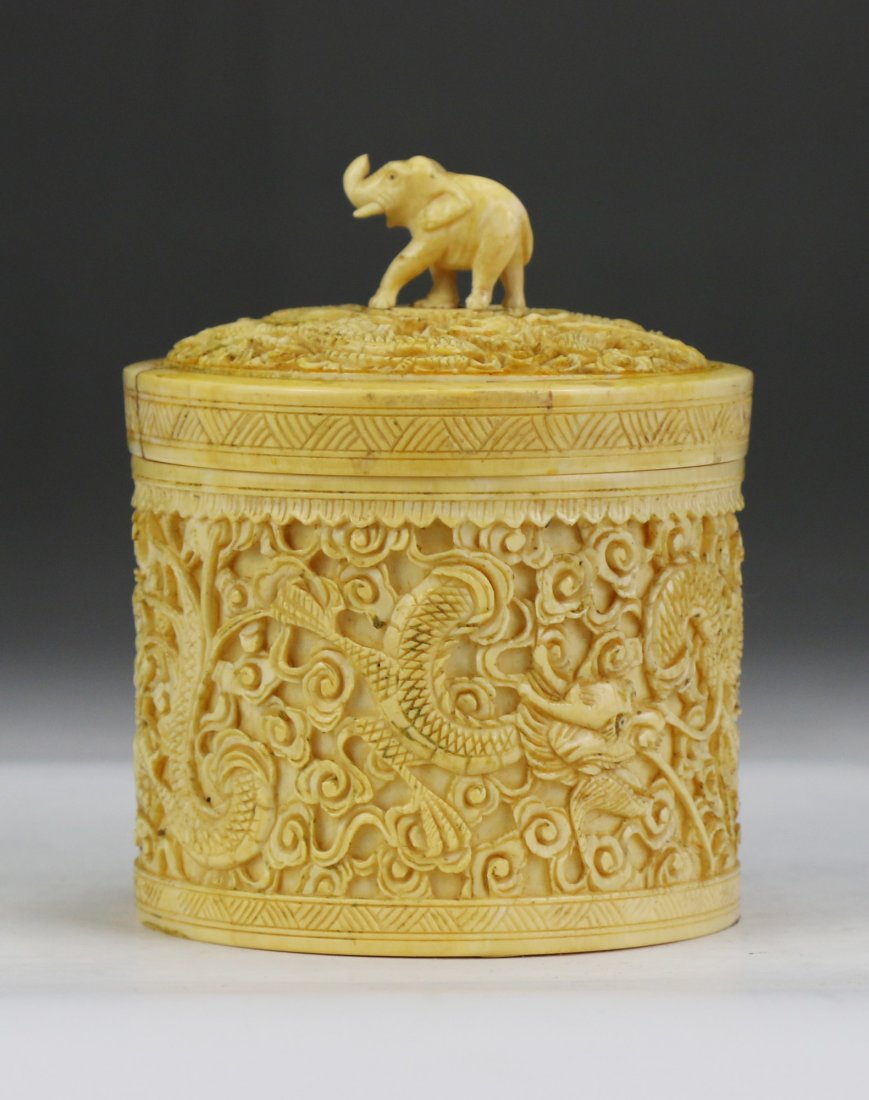 A Chinese Antique Ivory Carved Lidded Case: A Chinese Antique Ivory Carved Lidded Case: of cylindrical form, finely carved with dragons flying amid clouds around the body, the lid with an elephant carved finial at the center, African ivory, of 