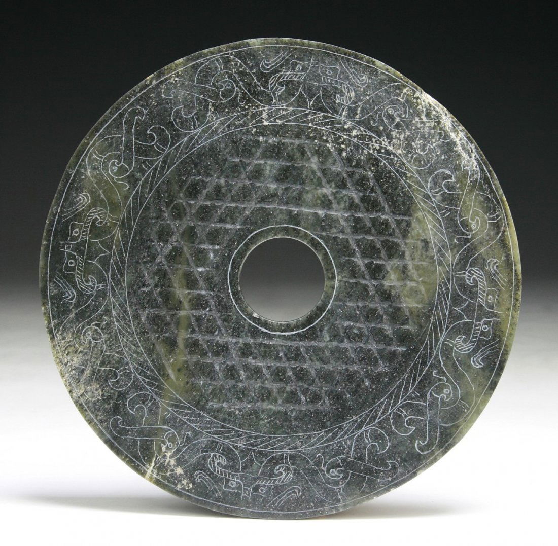 A Chinese Archaic Spinach Jade Bi: A Chinese Archaic Spinach Jade Bi: of flat circular form with a hole in the center, carved with motif of archaic dragon designs, of Western Han Dynasty; Size: D: 6-1/4"