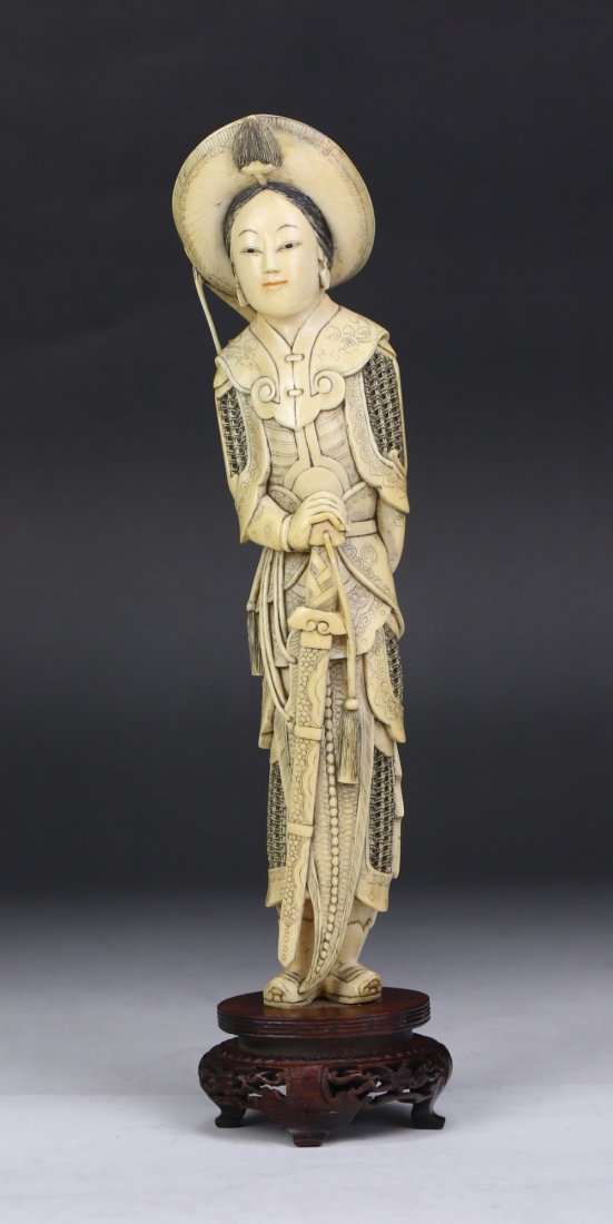 A Chinese Antique Ivory Carved Figure Of Mulan: A Chinese Antique Ivory Carved Figure Of Mulan: finely carved as Mulan standing in a warrior robe wearing a head dress while holding a long sword, presented on a wood stand, African ivory, Late Qing D