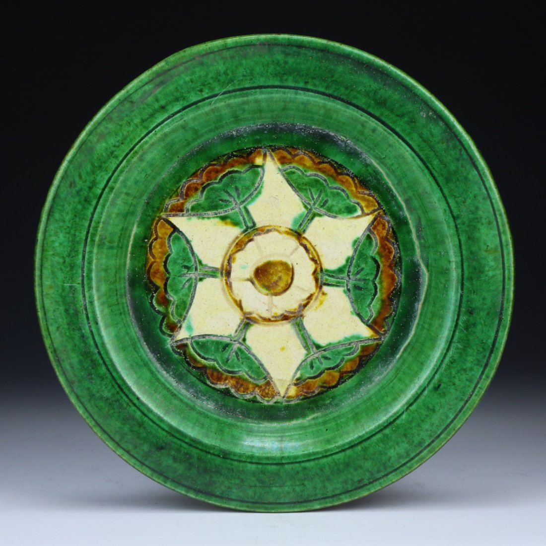A Chinese Antique SANCAI-Glazed Pottery Plate: A Chinese Antique SANCAI-Glazed Pottery Plate: of shallow form, impressed in the center with a flower head in amber, green and cream glaze reserved on a green glaze that continues over the rim to part