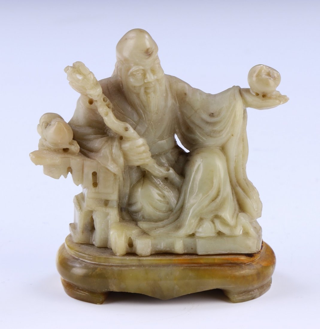 A Chinese Antique Shoushan Soapstone Shoulao: 壽山石雕壽老A Chinese Antique Shoushan Soapstone Shoulao: Shown Seated On A Simulated Rockwork Dais Of Beige, Ochre And Russet Tone, The Shoulao Depicted With A Pla