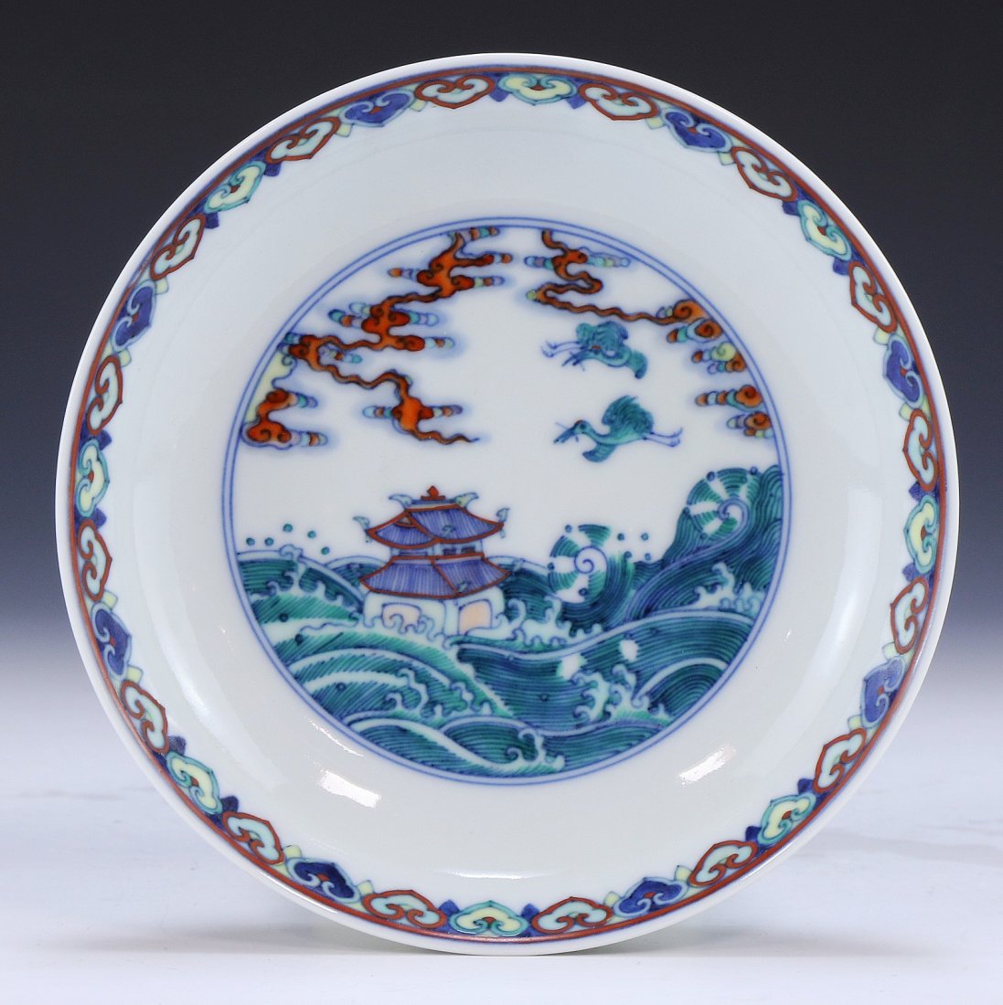 A CHINESE ANTIQUE DOUCAI PORCELAIN SAUCER: A Chinese Antique Doucai Porcelain Saucer: The interior Finely Painted With A Temple in Scrolling Waves With Birds Flying Above, The Back With Blossoms And Foliate, At The Center Sealed With A Qianlon