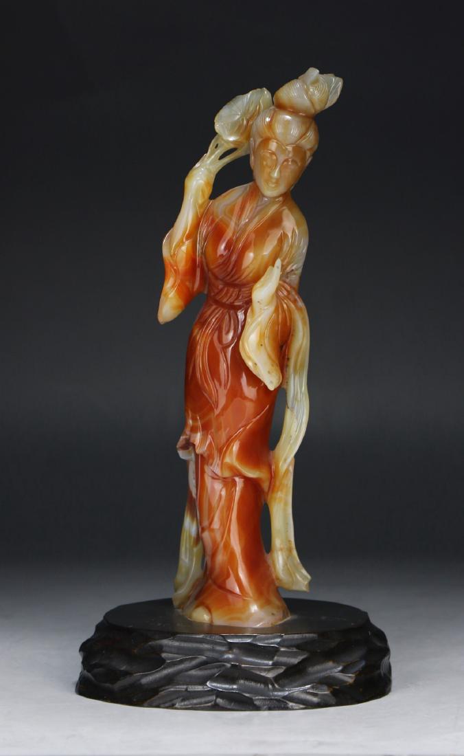 A CHINESE JADEITE CARVED BEAUTY: A Chinese Jadeite Carved Beauty: Finely Carved As A Beauty in Flowing Robes Holding A Lily Pad, The Jadeite Of Mottled Pale Green To Red Tones, Presented On A Wood Stand; Size: H: 9-3/4" (24.77cm)