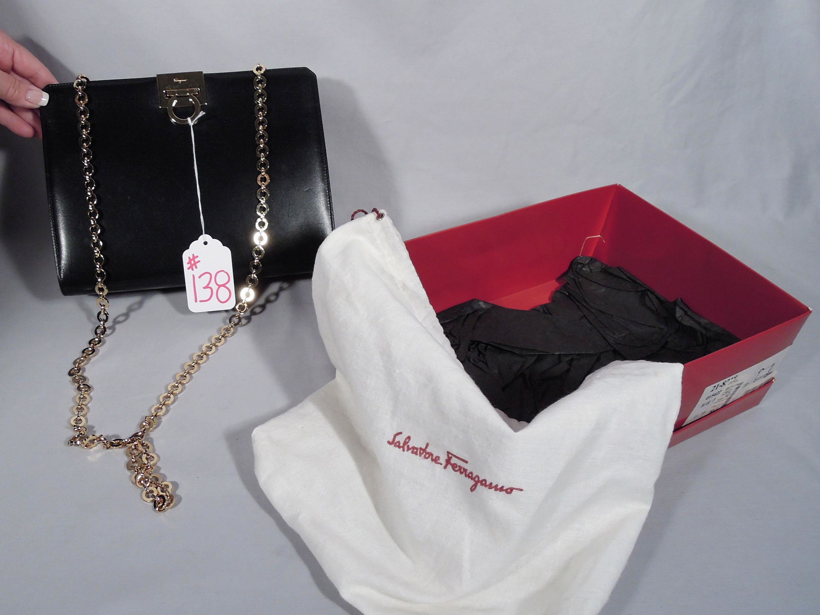 SALVATORE FERRAGAMO HAND BAG: Black purse with gold chain and clasp. 7 1/2" high, 10" wide. We are not experts in hand bags so please review all photos and make your own determination.