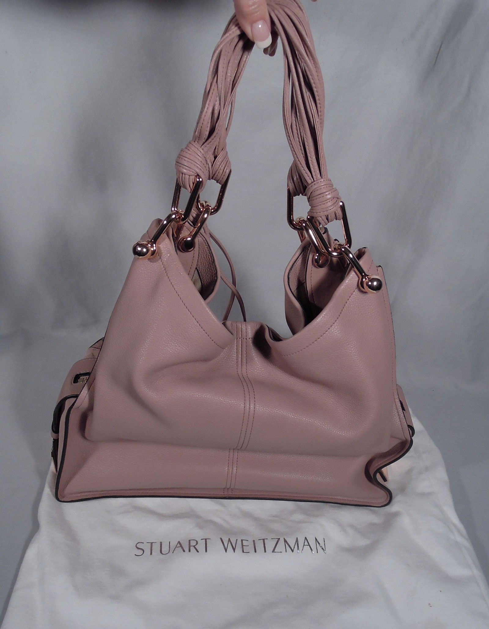 STUART WEITZMAN MAUVE LEATHER PURSE: Rose gold colored decorations and multi strand straps. 13" high, 15" wide. Very good condition. We are not experts in hand bags so please review all photos and make your own determination.