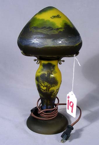 ACID ETCHED CAMEO GLASS LAMP: ACID ETCHED CAMEO GLASS LAMP A bulbous base supports a mushroom shaped shade. Landscape scene in purple and gold coloration. Signed. Base and top both electrified. 13” high, 6 1/4” dia.