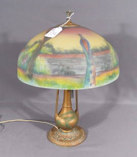BEAUTIFUL ART DECO GILT METAL AND REVERSE PAINTED TABLE LAMP: An Art Deco base supports a domed resverse painted shade with peacock and garden motif. Note: Two small chips on edge of shade. 22" high, 16 1/2" dia.