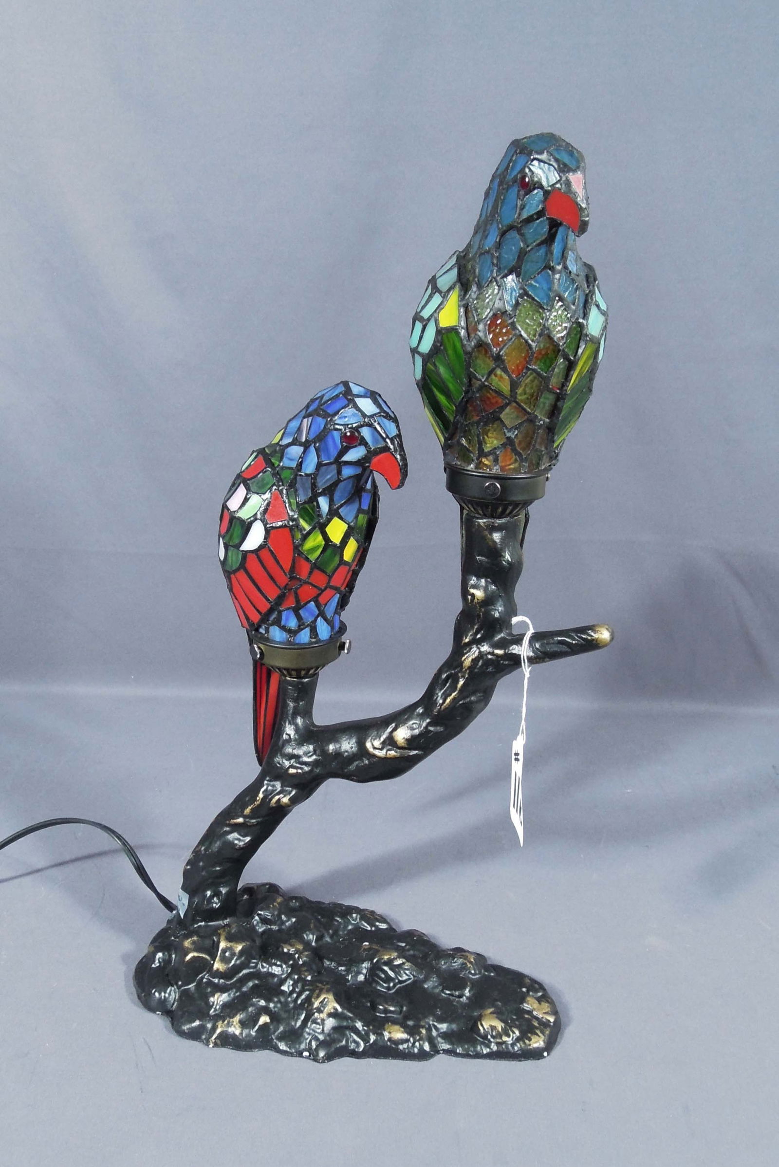 HAND PAINTED COMPOSITION AND LEADED GLASS "PARROT" TABLE LAMP: Two colorful leaded glass parrots perched on branch. 22" high, 12" wide, 6 3/4" deep.