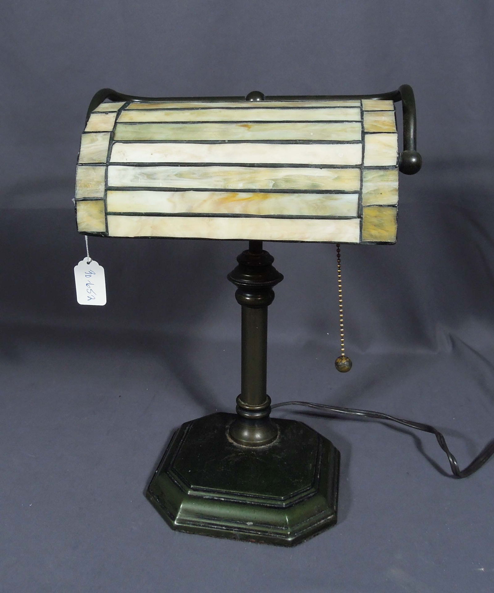 METAL AND LEADED GLASS BANKER'S LAMP: A metal base supports an adjustable leaded glass shade. 15" high, 10 1/2" wide, 6 3/4" deep.