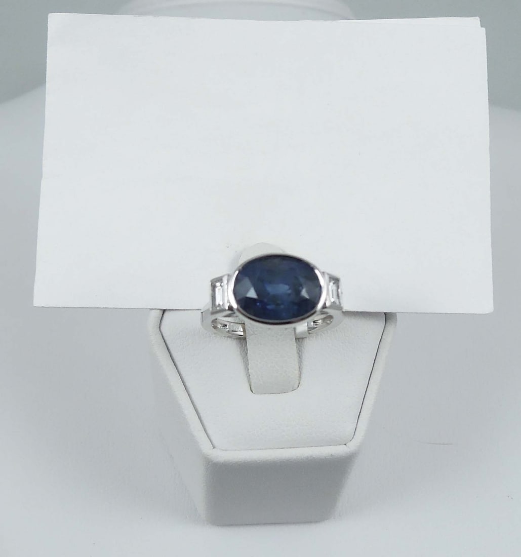 LADIES PLATINUM, NATURAL BLUE SRILANKA SAPPHIRE & DIAMOND RING: A platinum mount is set with an oval cut GIA certified Srilankan sapphire weighing approx. 5.96 cts. Ring completed with two baguette cut diamonds totaling approx. .29 ct. Diamonds VSI-VS2 clarity, F-