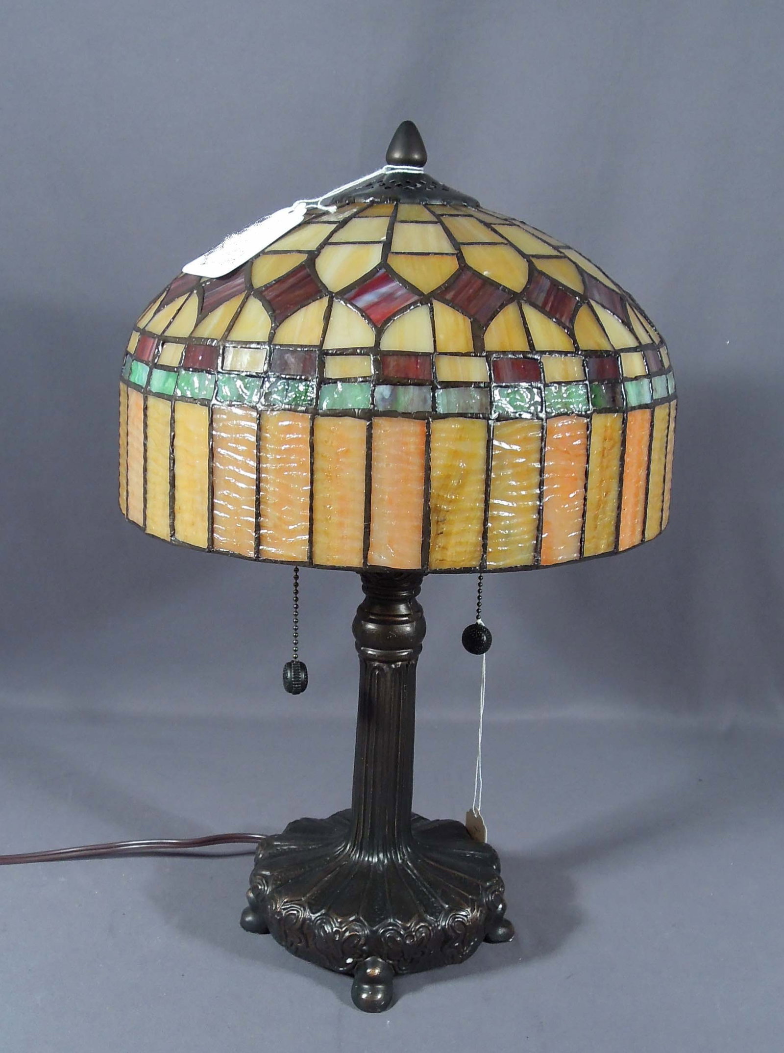 FINE TIFFANY STYLE METAL AND LEADED GLASS TABLE LAMP: Ornate four footed base suports a domed carmel, brown & green leaded glass shade. Excellent condtion. 19" high, 12" dia.
