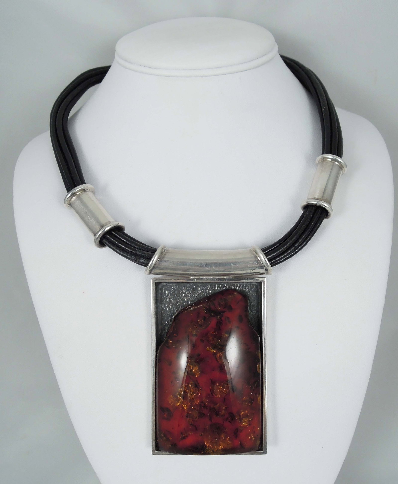 DESIGNER MARIUSZ GLIWINSKI (POLISH) STERLING SILVER, LEATHER AND AMBER NECKLACE: A multi strand leather necklace with sterling silver sections supports a large sterling silver pendant inset with a large free form amber. Pendant 3" x 2".